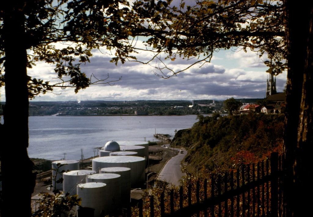Photographie récente de l'Anse au Foulon — lieu de passage des troupes anglaises dans la nuit du 12 au 13 septembre 1759, menant à la bataille des Plaines d'Abraham, puis site d'importance pour le commerce du bois au XIXe siècle. En 1927, le Port de Québec y a déversé du sable pour accueillir de plus gros navires; de 1930 à 1960 c'était une plage fréquentée. Dans les années 1960, pollution et construction du boulevard Champlain ont mis fin à la baignade. On y voit les silos blancs construits en 2013. © Société d'histoire de Sillery